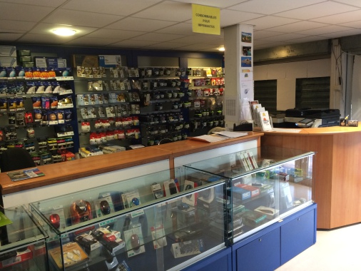 une vue du comptoir. Le matériel : ordinateurs, périphériques, tablettes, imprimantes, accessoires réseau, câbles usb, hdmi, DP, est présenté dans des vitrines rétroéclairée dans une teinte bleue.