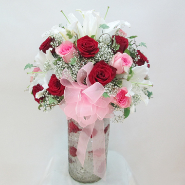 An arrangement of white lilies mixed with imported red and pink roses in a glass vase.